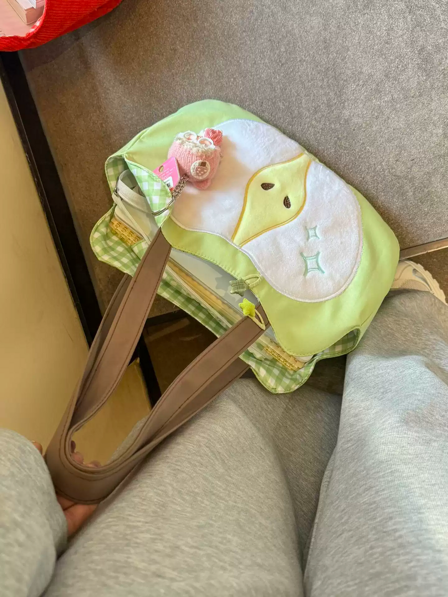 小さなぬいぐるみチャームと一緒にグレーのソファに置かれたグリーンPomiバッグ